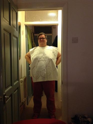 A dyke wears a tabard with a drawing of a cock on it